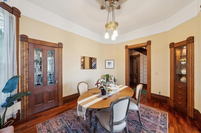 dining space with a notable chandelier, dark wood-type flooring, and a raised ceiling