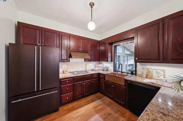 kitchen featuring pendant lighting, sink, black appliances, light stone countertops, and light hardwood / wood-style flooring