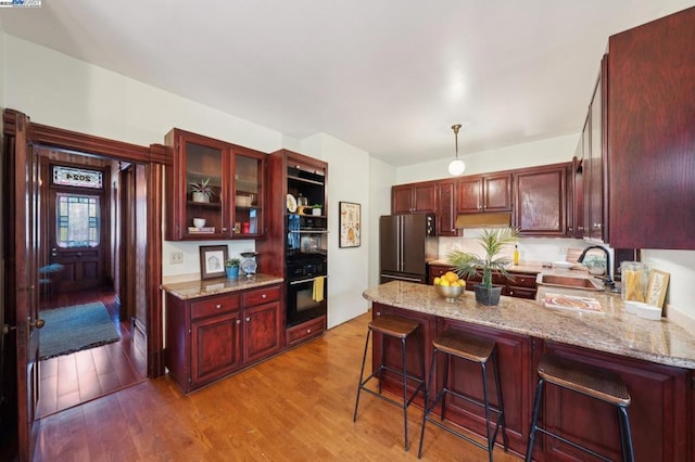 kitchen with sink, a breakfast bar area, light stone counters, light hardwood / wood-style flooring, and high quality fridge