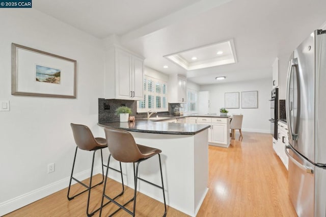 kitchen with a raised ceiling, white cabinetry, stainless steel refrigerator, and kitchen peninsula