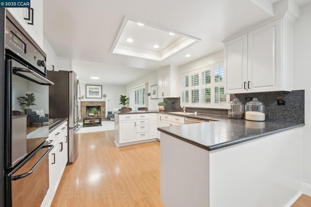 kitchen featuring a tray ceiling, kitchen peninsula, light hardwood / wood-style flooring, and white cabinets