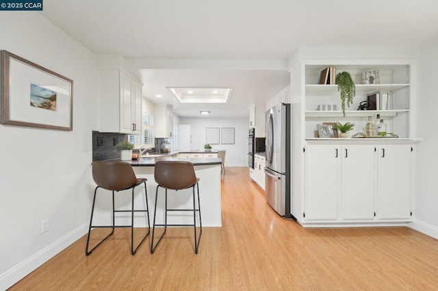 kitchen with white cabinetry, light hardwood / wood-style flooring, stainless steel refrigerator, kitchen peninsula, and a raised ceiling