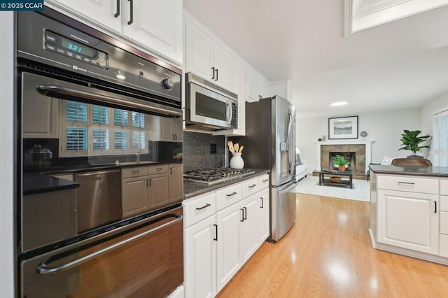 kitchen with tasteful backsplash, stainless steel appliances, white cabinets, and light wood-type flooring