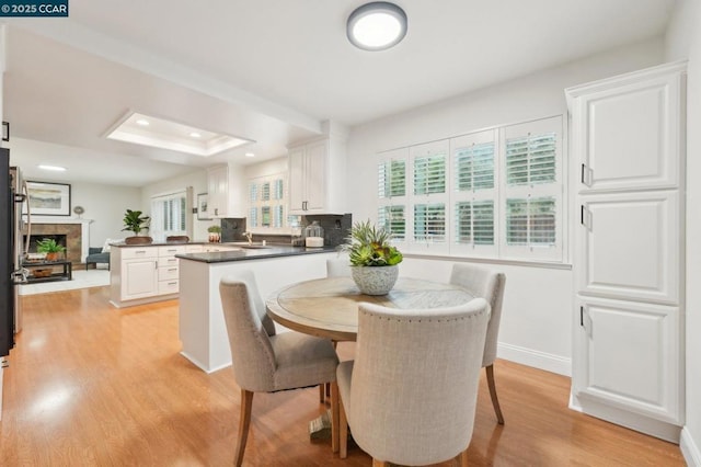 dining room with sink, a raised ceiling, and light wood-type flooring