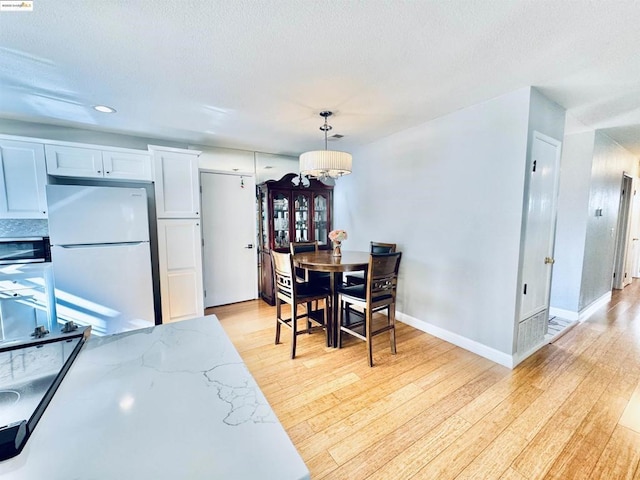 dining area featuring an inviting chandelier, light hardwood / wood-style flooring, and a textured ceiling