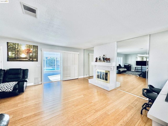 living room with a brick fireplace, light hardwood / wood-style flooring, and a textured ceiling