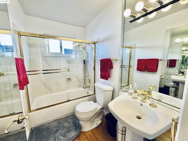 full bathroom featuring combined bath / shower with glass door, sink, hardwood / wood-style floors, and toilet