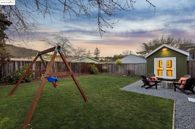 yard at dusk with an outdoor fire pit, an outdoor structure, a playground, and a patio