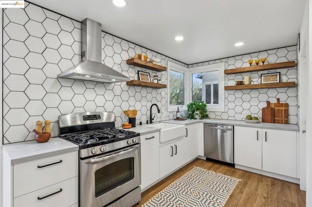 kitchen with wall chimney exhaust hood, sink, white cabinets, stainless steel appliances, and backsplash