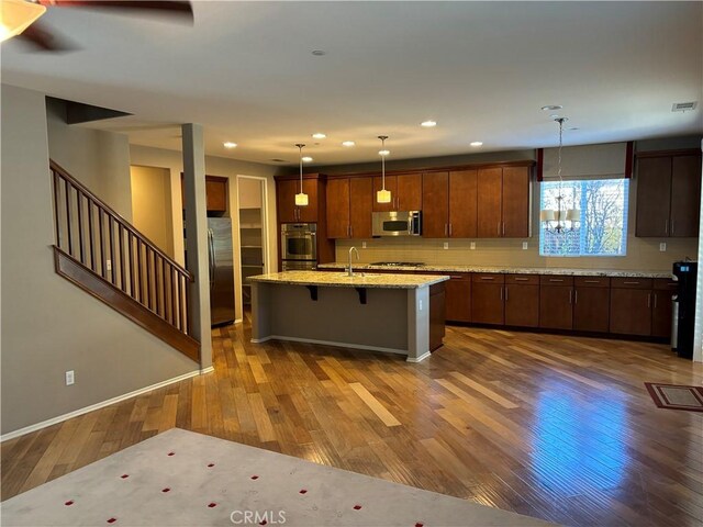 kitchen featuring decorative light fixtures, a kitchen breakfast bar, dark hardwood / wood-style floors, stainless steel appliances, and a kitchen island with sink