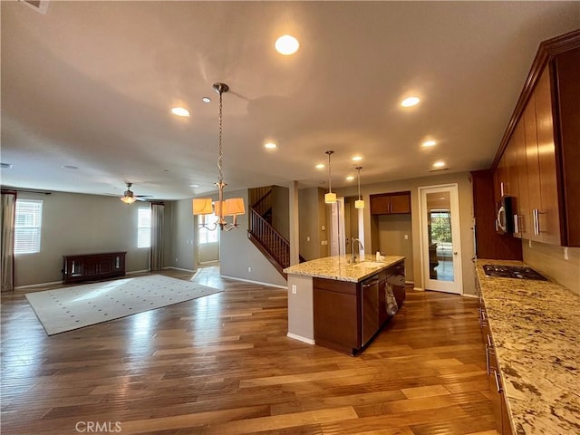 kitchen with light stone counters, hanging light fixtures, dark hardwood / wood-style floors, an island with sink, and stainless steel appliances