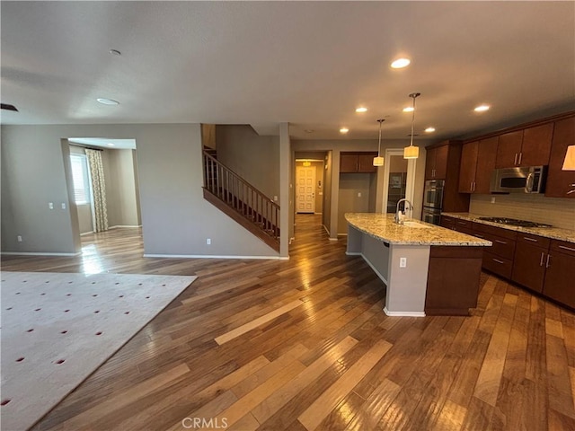 kitchen featuring stainless steel appliances, light stone countertops, dark hardwood / wood-style floors, and a center island with sink