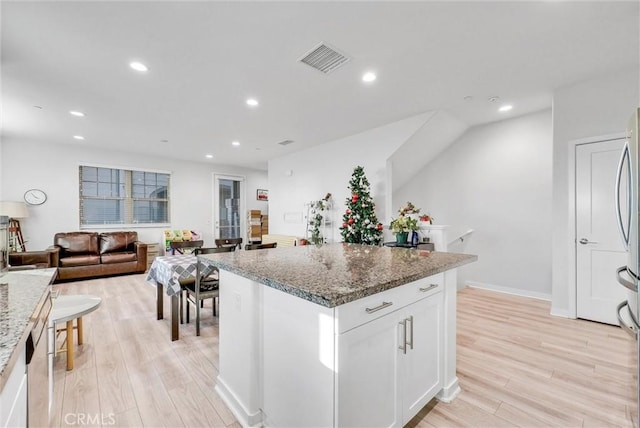 kitchen with white cabinetry, light stone countertops, a kitchen island, and light wood-type flooring