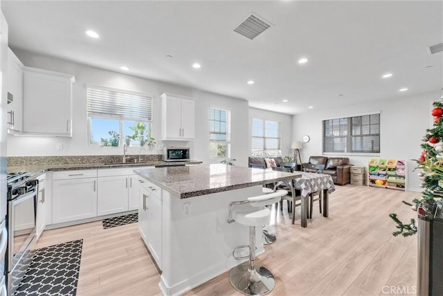 kitchen featuring sink, a center island, light wood-type flooring, dark stone countertops, and white cabinets