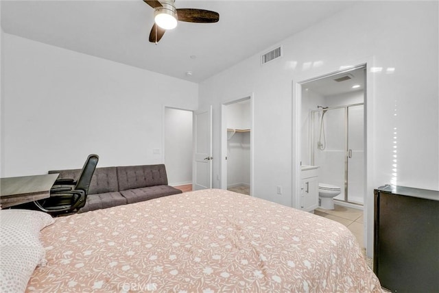 tiled bedroom with ceiling fan, a walk in closet, ensuite bathroom, and a closet