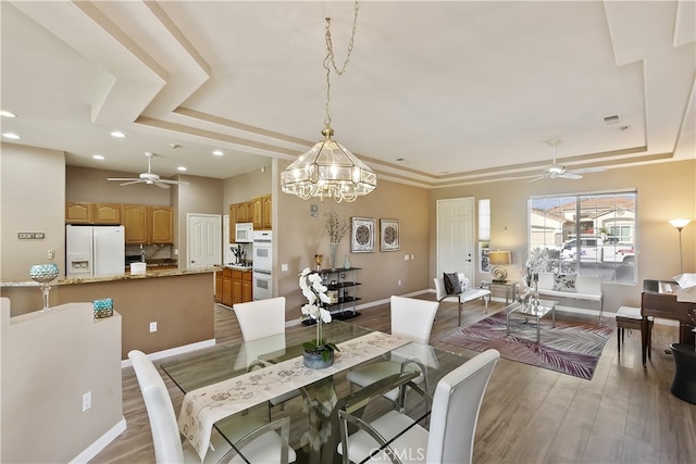 dining room with light hardwood / wood-style flooring, ceiling fan, and a tray ceiling