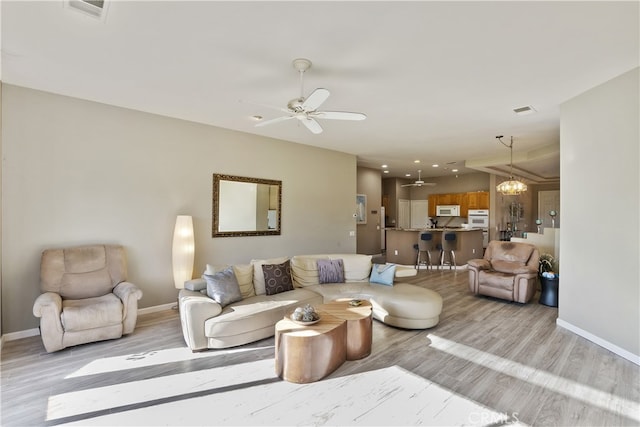 living room featuring ceiling fan with notable chandelier and light wood-type flooring