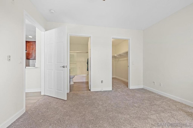 unfurnished bedroom with a spacious closet, light colored carpet, a closet, and ensuite bathroom