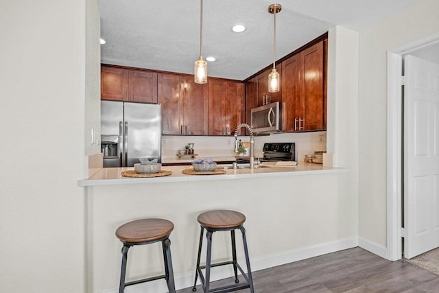 kitchen with appliances with stainless steel finishes, dark hardwood / wood-style floors, pendant lighting, and kitchen peninsula