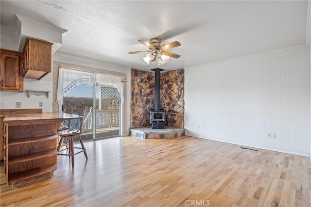 living room featuring crown molding, ceiling fan, light hardwood / wood-style floors, and a wood stove