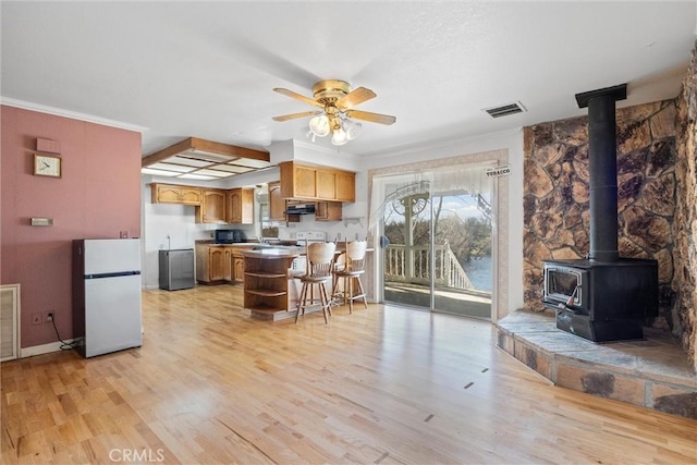 kitchen featuring refrigerator, a wood stove, a kitchen breakfast bar, ceiling fan, and light hardwood / wood-style floors