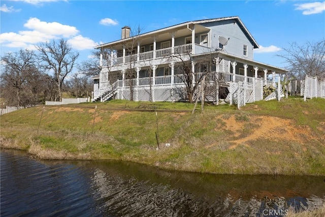 back of property featuring a porch, a balcony, a water view, and a lawn