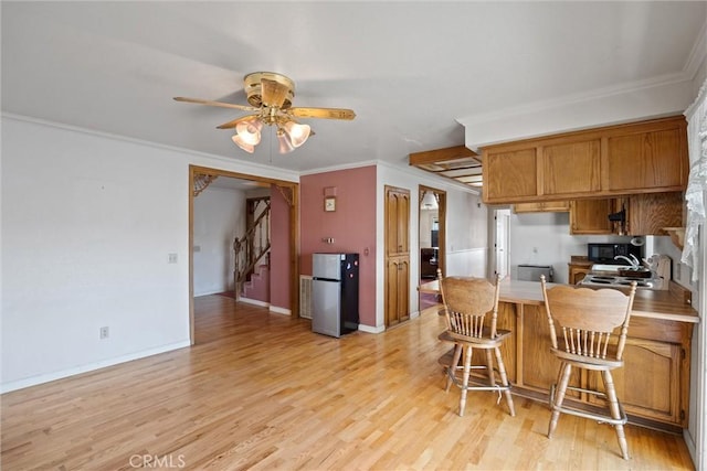 kitchen with light hardwood / wood-style flooring, ornamental molding, stainless steel refrigerator, and a kitchen bar