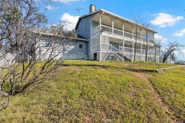 rear view of house featuring a balcony and a yard