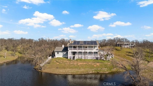 rear view of house featuring a water view, a yard, and solar panels