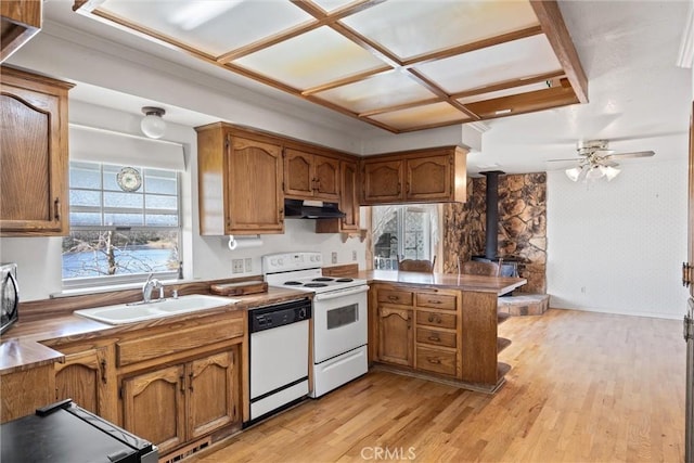 kitchen with sink, a wood stove, kitchen peninsula, white appliances, and light hardwood / wood-style floors