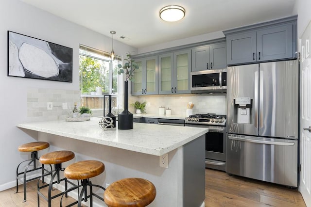 kitchen featuring dark wood-type flooring, a breakfast bar, light stone counters, appliances with stainless steel finishes, and backsplash