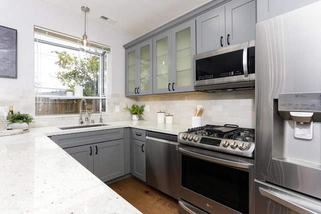 kitchen with sink, light stone counters, tasteful backsplash, appliances with stainless steel finishes, and pendant lighting