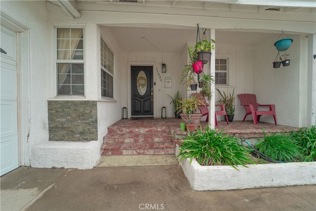 view of exterior entry with covered porch, a garage, and stucco siding