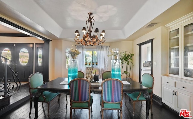 dining room with an inviting chandelier, dark wood-type flooring, and a raised ceiling