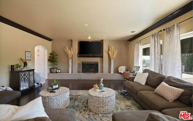 living room featuring hardwood / wood-style flooring, ornamental molding, brick wall, and a brick fireplace