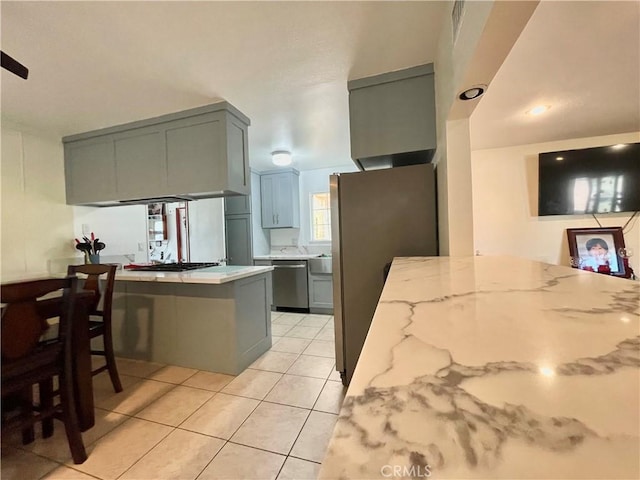 kitchen featuring a breakfast bar, stainless steel appliances, light stone countertops, light tile patterned flooring, and kitchen peninsula