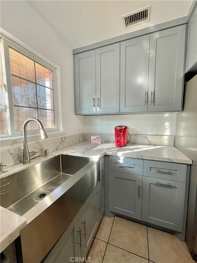 kitchen with light tile patterned floors, light stone countertops, sink, and gray cabinetry