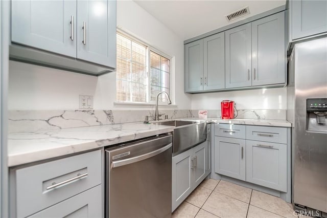 kitchen with sink, light tile patterned floors, gray cabinetry, stainless steel appliances, and light stone countertops