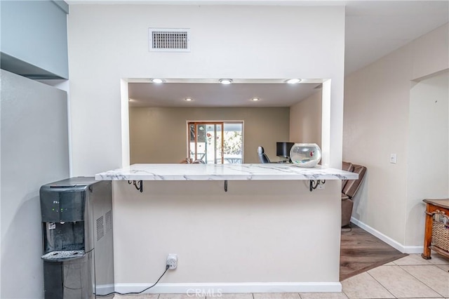 kitchen featuring light stone counters, light tile patterned floors, kitchen peninsula, and a kitchen bar