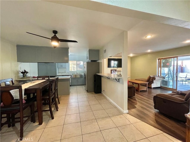 kitchen featuring light tile patterned flooring, light stone countertops, stainless steel fridge, and ceiling fan