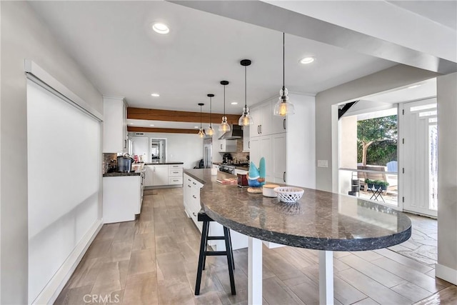 kitchen featuring hanging light fixtures, light wood-type flooring, white cabinets, wall chimney range hood, and backsplash