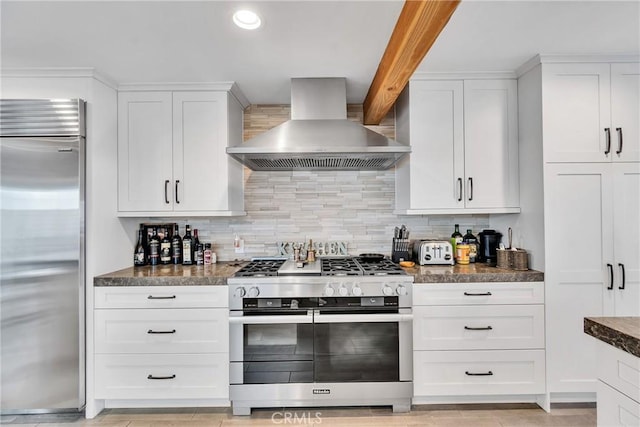 kitchen featuring stainless steel appliances, tasteful backsplash, wall chimney range hood, and white cabinets