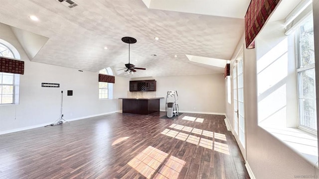 unfurnished living room with dark wood-type flooring, vaulted ceiling with skylight, and ceiling fan