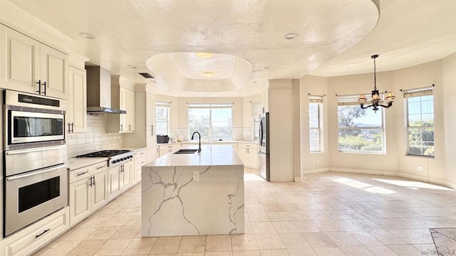 kitchen featuring sink, a center island with sink, gas cooktop, pendant lighting, and wall chimney range hood