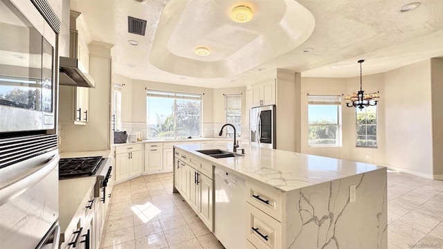 kitchen featuring a spacious island, sink, light stone counters, decorative light fixtures, and stainless steel appliances