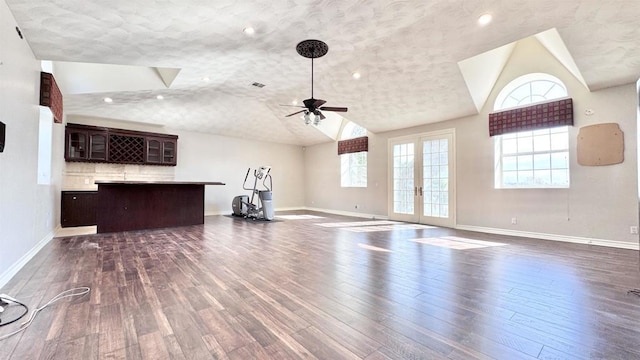 unfurnished living room featuring vaulted ceiling, a wealth of natural light, dark hardwood / wood-style flooring, and french doors