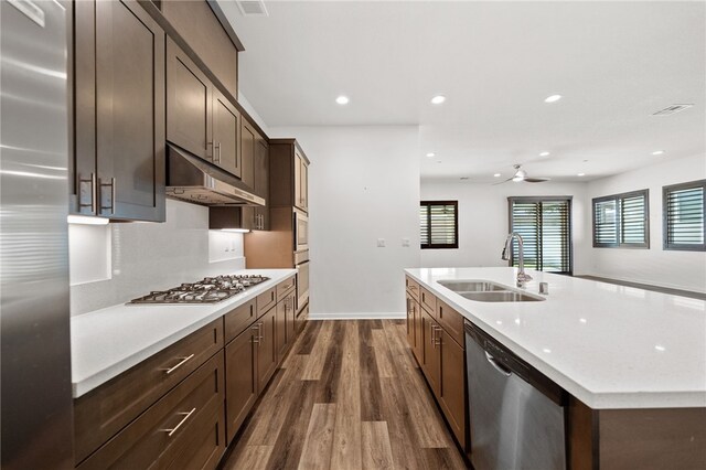 kitchen featuring sink, dark brown cabinets, stainless steel appliances, dark hardwood / wood-style floors, and a center island with sink