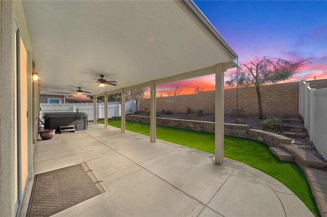 patio terrace at dusk with a hot tub, ceiling fan, and a lawn