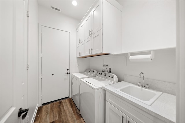 laundry area featuring sink, dark hardwood / wood-style floors, washing machine and dryer, and cabinets