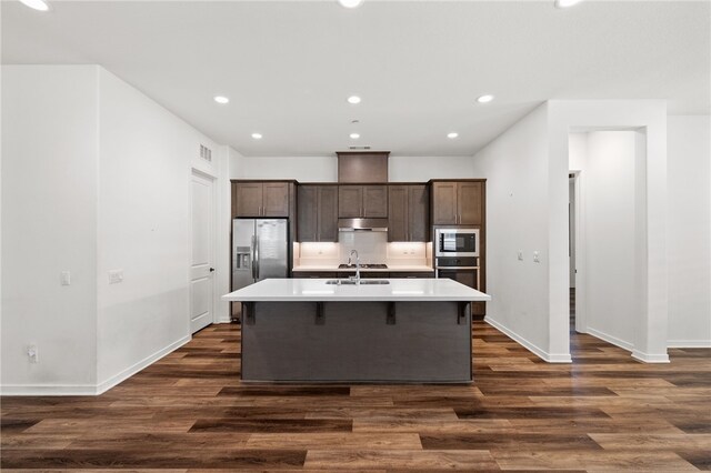 kitchen featuring stainless steel appliances, an island with sink, a kitchen breakfast bar, and dark hardwood / wood-style flooring